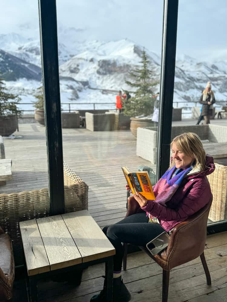 A woman reading a book on a balcony overlooking the mountains.