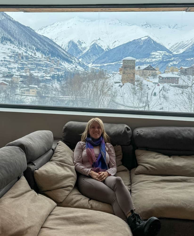 A woman sitting on a couch in front of a window with snow covered mountains.