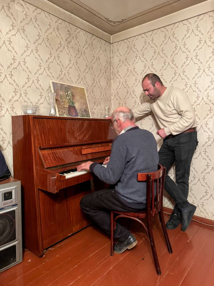 Two men playing a piano in a room.