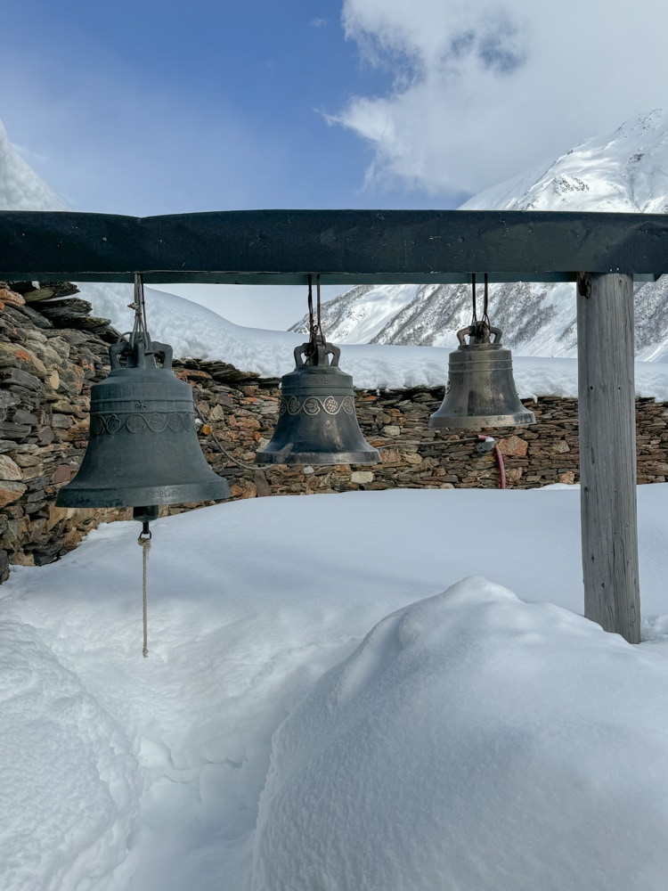 Bells in a snow covered area with mountains in the background.