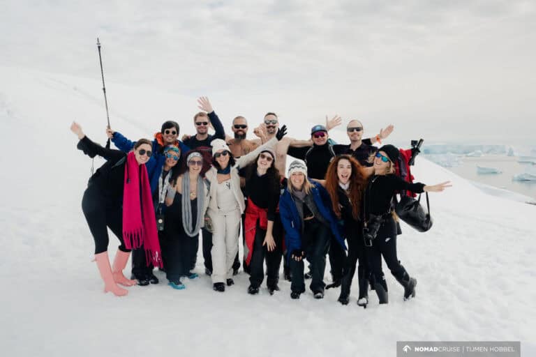 A group of joyful people in varied attire posing together on a snowy landscape with icebergs in the background.