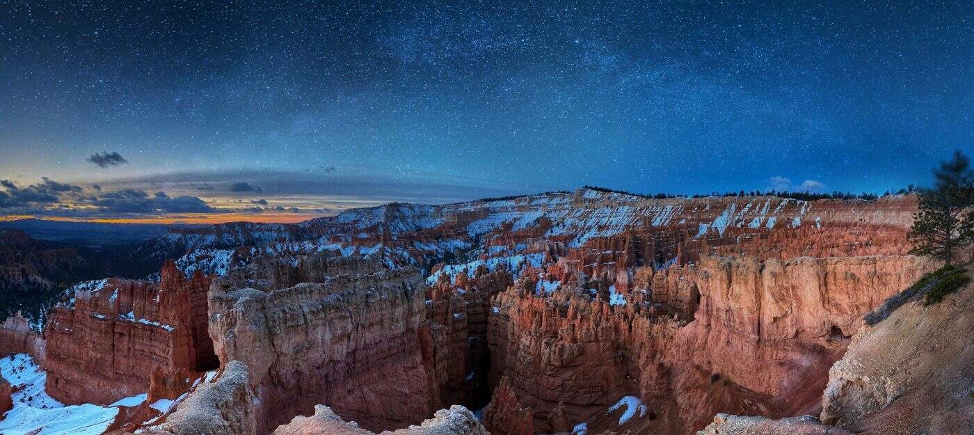A panoramic view of Bryce Canyon with snow-dusted red rock formations under a clear, starry night sky.